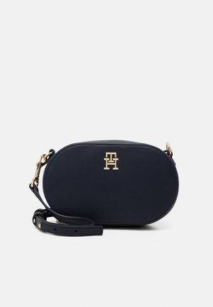 Pieni ovaalinmuotoinen musta nahkainen crossbody-laukku, jossa säädettävä hihna ja edessä kultasävyinen merkin logo.