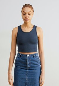Cropped dark gray tank top made of ribbed material, paired with a high-waisted blue denim skirt featuring a front seam and button closure.