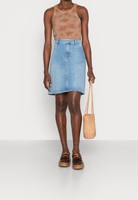 Jeanskjol i ljusblått med rak skärning och lätt slitning vid fållen, tillsammans med en brun batikmönstrad linne och bruna skor.