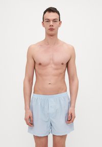 Boxers en coton bleu clair avec une taille élastique et une fermeture à bouton à l'avant, portés par un modèle avec une expression neutre.