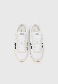 Para białych sneakersów Tommy Hilfiger z beżowymi i czarnymi akcentami, związanych sznurówkami i ustawionych obok siebie na białym tle.