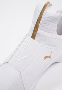 Białe buty sportowe Puma z złotym logo Puma i uchwytem, teksturowana cholewka oraz design slip-on.