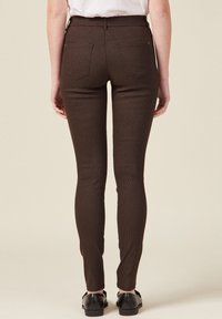 Pantalones skinny de color marrón con un estampado, talle alto y diseño de cinco bolsillos. Textura suave, forma ajustada y largo hasta los tobillos. Zapatos negros visibles.