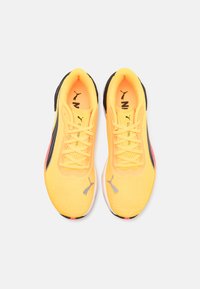 Scarpe da atletica gialle brillanti con accenti neri, upper in mesh testurizzato, lacci piatti e logo Puma grigio sulla punta e sul lato.