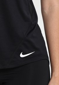 T-shirt de sport noir avec une coupe ajustée, une texture lisse et un logo Nike blanc près de l'ourlet. Tissu respirant avec des accents en mesh.