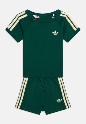 Ciemnozielony zestaw z krótkim rękawem i szortami z kremowymi paskami na rękawach i bokach, z logo Adidas na piersi i szortach.