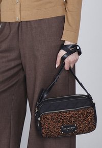 Bolso de mano negro y naranja con parte superior acolchada, tela de patrón espiga, dobles compartimentos con cremallera y una correa desmontable.