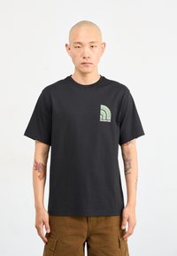 Sort bomulds t-shirt med et grønt grafisk design på venstre bryst. Korte ærmer og en klassisk rund hals. Glat tekstur.