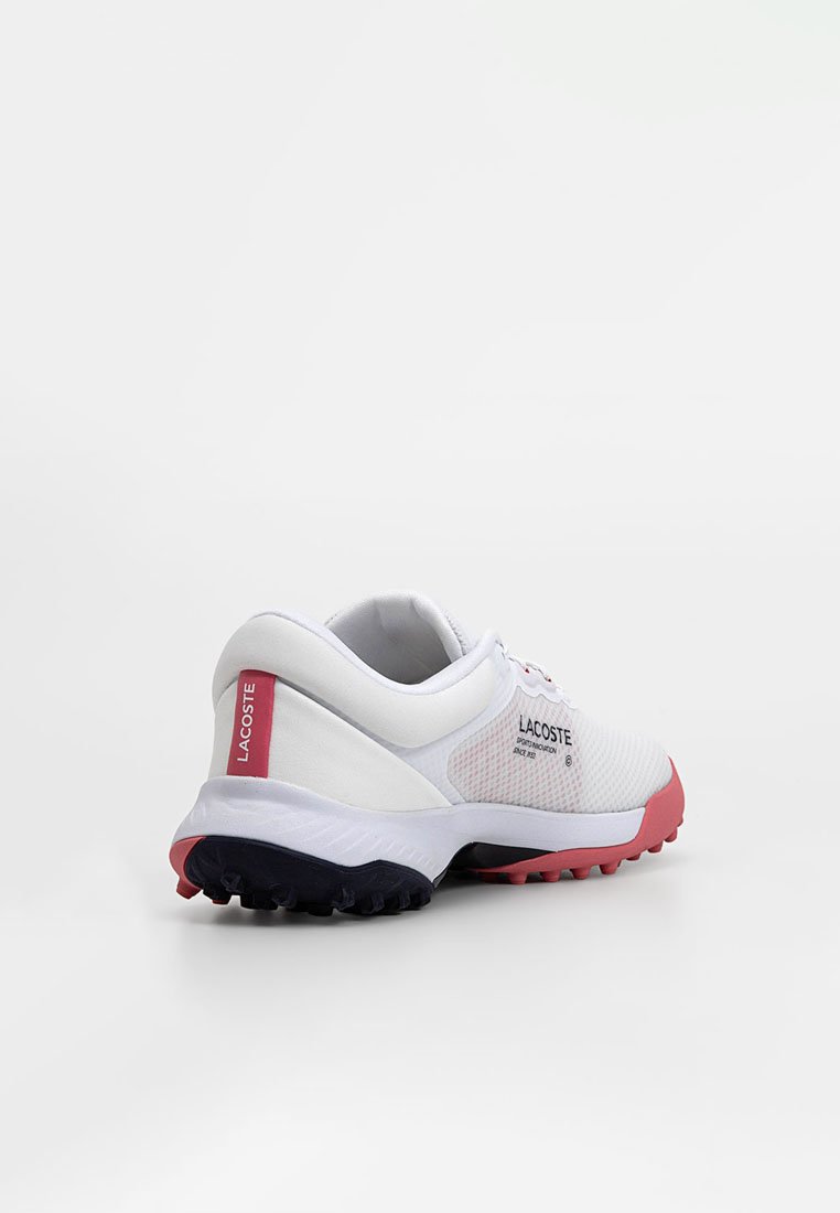 Zapatilla Lacoste blanca con tachuelas rojas y negras en la suela, tirador rojo en el talón y logotipo en el lateral, en un ángulo que muestra la parte trasera y el lado exterior.