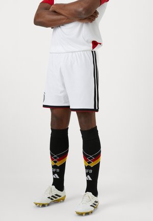 Hvide fodboldshorts med sorte striber, parret med sorte sokker med røde, gule og sorte diamantmønstre, samt hvide fodboldstøvler.