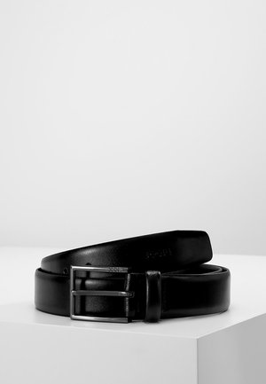 Ceinture en cuir noir avec une boucle rectangulaire en argent, texture lisse, et logo de marque visible embossé sur la sangle.