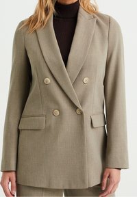 Beige dubbelknäppt blazer med skräddarsydd passform, två framfickor och ljusa knappar. Tillverkad av strukturerad tyg som ger en väldefinierad look.