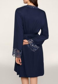 Granatowy szlafrok wykonany z miękkiego materiału, ozdobiony koronkowymi wykończeniami na rękawach i dekolcie, związany w talii dopasowanym paskiem.