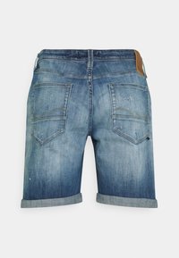 Denimshorts i ljusblått med en blekt tvätt. Har uppvikta fållar, två bakfickor och en brun läderpatch vid midjan.
