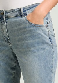 Jeans de mezclilla azul claro con una textura suave, que presentan un diseño clásico de cinco bolsillos y un sutil patrón desgastado.