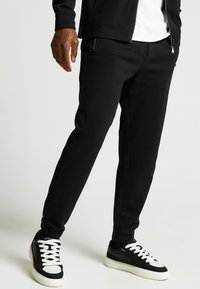 Zwarte joggerbroeken van zachte stof, met slim fit, elastische boorden en zijzakken. gedragen met zwart-witte sneakers.