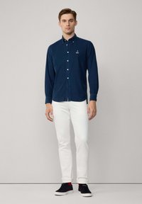 Marineblauw knoopshirt met lange mouwen, gemaakt van zacht materiaal. Gekocht in combinatie met witte slim-fit jeans en zwarte sneakers met rode accenten.