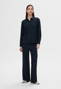 Sötét tengerészkék két részes ruházat, amely gombos hosszú ujjú inget és bő szárú nadrágot tartalmaz, mindkettő sima anyagból, laza szabással készült.