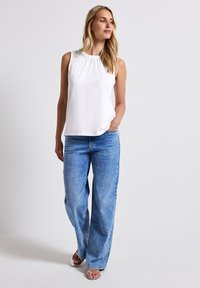 White sleeveless top with pleated neckline, paired with light blue wide-leg jeans and silver strappy sandals. Neutral background.