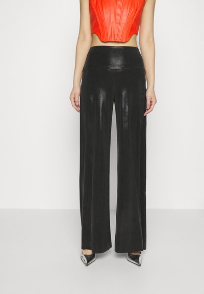 Pantalones negros de cintura alta y pierna ancha con un acabado brillante, combinados con un top corto rojo brillante. El conjunto incluye unos tacones metálicos de punta.