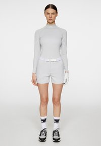 Ljusgrå långärmad topp och shorts, vit texturerad bälte, vita handskar, svart och vita sportstrumpor, svarta träningsskor.