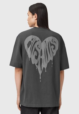 T-shirt gris surdimensionné avec un grand graphique en forme de cœur dégoulinant à l'arrière en gris clair, présentant un texte en gras et stylisé.