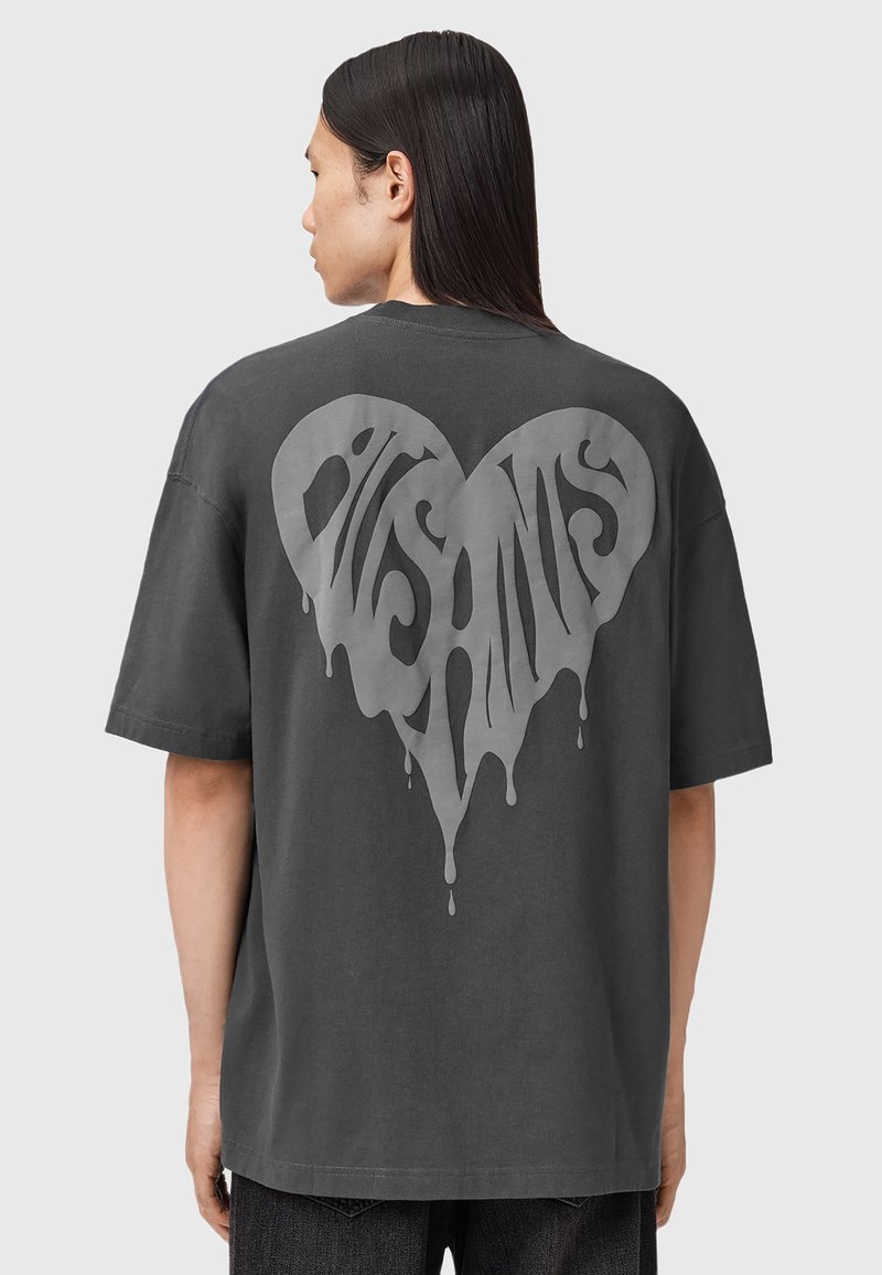 Camiseta gris de gran tamaño con un gran gráfico en forma de corazón goteante en la parte trasera en un gris más claro, que presenta un texto audaz y estilizado.