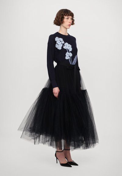 Navy sweater with floral embroidery paired with a black tulle skirt, featuring a fitted waist and bow detail, worn with black stiletto heels.