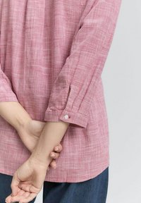 Chemise à carreaux rouge et blanc avec une coupe décontractée, manches longues, poignets à boutons et un tissu texturé. Portée avec un jean en denim.