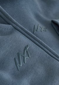 Granatowy materiałowy sweatshirt o miękkiej fakturze, zdobiony wypukłym logo w dopasowanym odcieniu niebieskiego. Design zawiera subtelne szwy i detale.