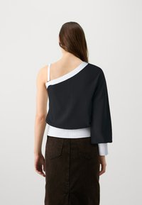 Haut en tricot noir avec une manche longue, des bordures blanches et une taille ajustée blanche, associé à une jupe marron foncé avec des poches arrières.