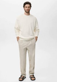 Light beige sweatshirt, cream trousers, and black sandals. Casual fit with long sleeves and slightly loose pants. Simple, minimalist design.