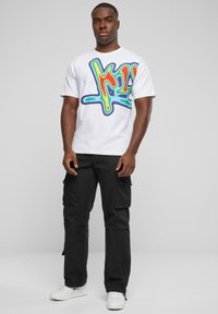 Hvitt bomullst-skjorte med en fargerik grafitti-inspirert grafikk; kombinert med svarte cargo-bukser og hvite sneakers. Enkelt design, avslappet passform.