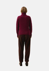 Burgundowy sweter z golfem w splot kabelkowy, z prążkowanym wykończeniem, w zestawieniu z brązowymi spodniami z korduroy i czarnymi botkami na grubej podeszwie.