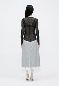 Čierny priesvitný top s dlhými rukávmi a vystupujúcimi bodkami, v kombinácii so svetlosivou sukňou s rázporkom vzadu; pod ním je vrstva bielej čipky.