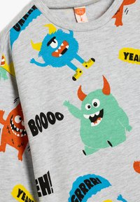 Sudadera gris con gráficos de monstruos coloridos en azul, verde, naranja y negro, con elementos de texto juguetones como "BOOO" y "¡YEAH!"