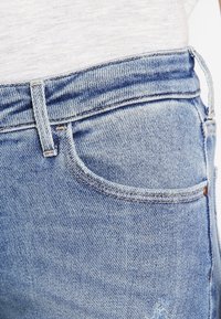 Jeans de mezclilla azul claro con un diseño clásico de cinco bolsillos, cintura alta y un ligero desgastado en la tela.