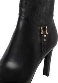 Stivaletto alla caviglia in pelle nera con motivo in rilievo sulla tomaia, dettagli in metallo dorato, punta appuntita e tacco a stiletto alto. Texture liscia.