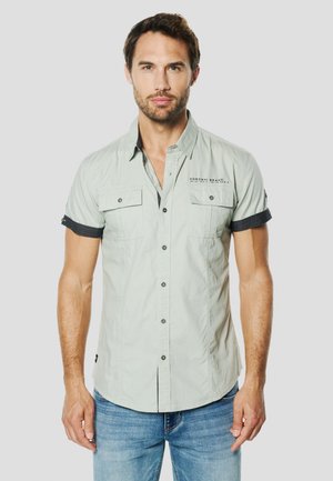 Cămașă verde deschis cu mânecă scurtă, două buzunare la piept, guler cu nasturi și accente negre pe mâneci. Confecționată din material ușor.