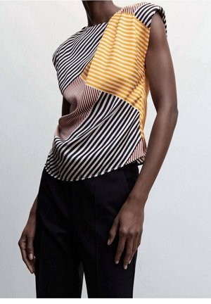 Haut sans manches avec des rayures diagonales et horizontales noires, blanches, jaunes et marron, porté avec un pantalon noir.