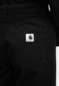 Μαύροι τζιν παντελόνια με εμφανές έμπλαστρο λογότυπου Carhartt ραμμένο στην πίσω δεξιά τσέπη.