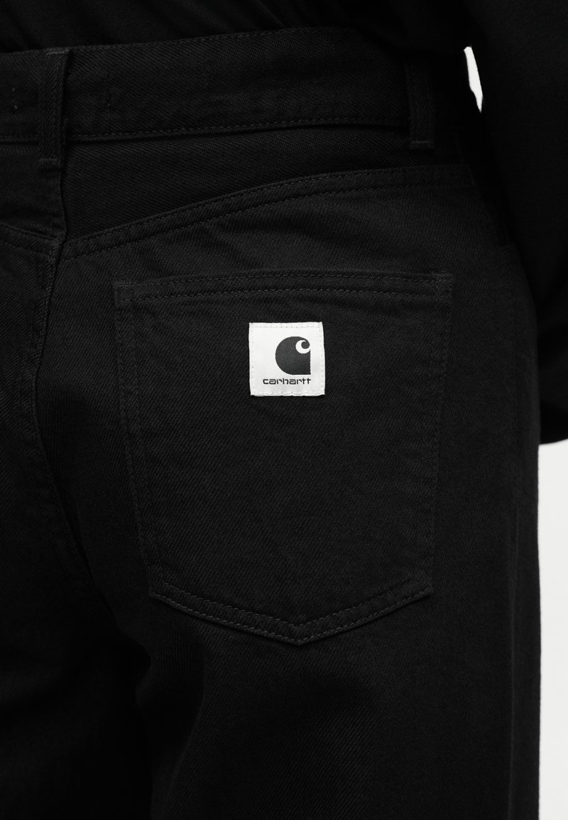 Zwarte spijkerbroek met een zichtbaar Carhartt-logo geborduurd op de rechterachterzak.