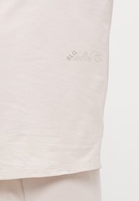 Hellbeige Baumwoll-T-Shirt mit abgerundetem Saum, das auf der unteren linken Seite bedruckten Text in einer kontrastierenden Farbe zeigt. Glatte Textur.