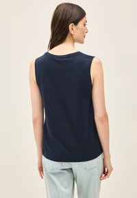 Top senza maniche in marina realizzato in morbido cotone, caratterizzato da un collo rotondo e una vestibilità rilassata, abbinato a pantaloni in denim chiaro.