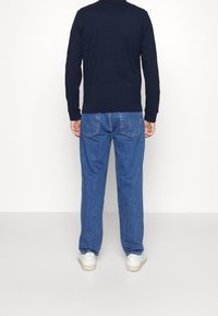 Sudadera texturizada azul marino con cuello redondo y puños acanalados, combinada con jeans de mezclilla azul claro, llevada con zapatillas blancas.