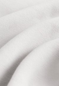 Gros plan sur un tissu blanc, doux et lisse, avec une texture de tissage fin visible et des plis légers créant un motif ondulé.