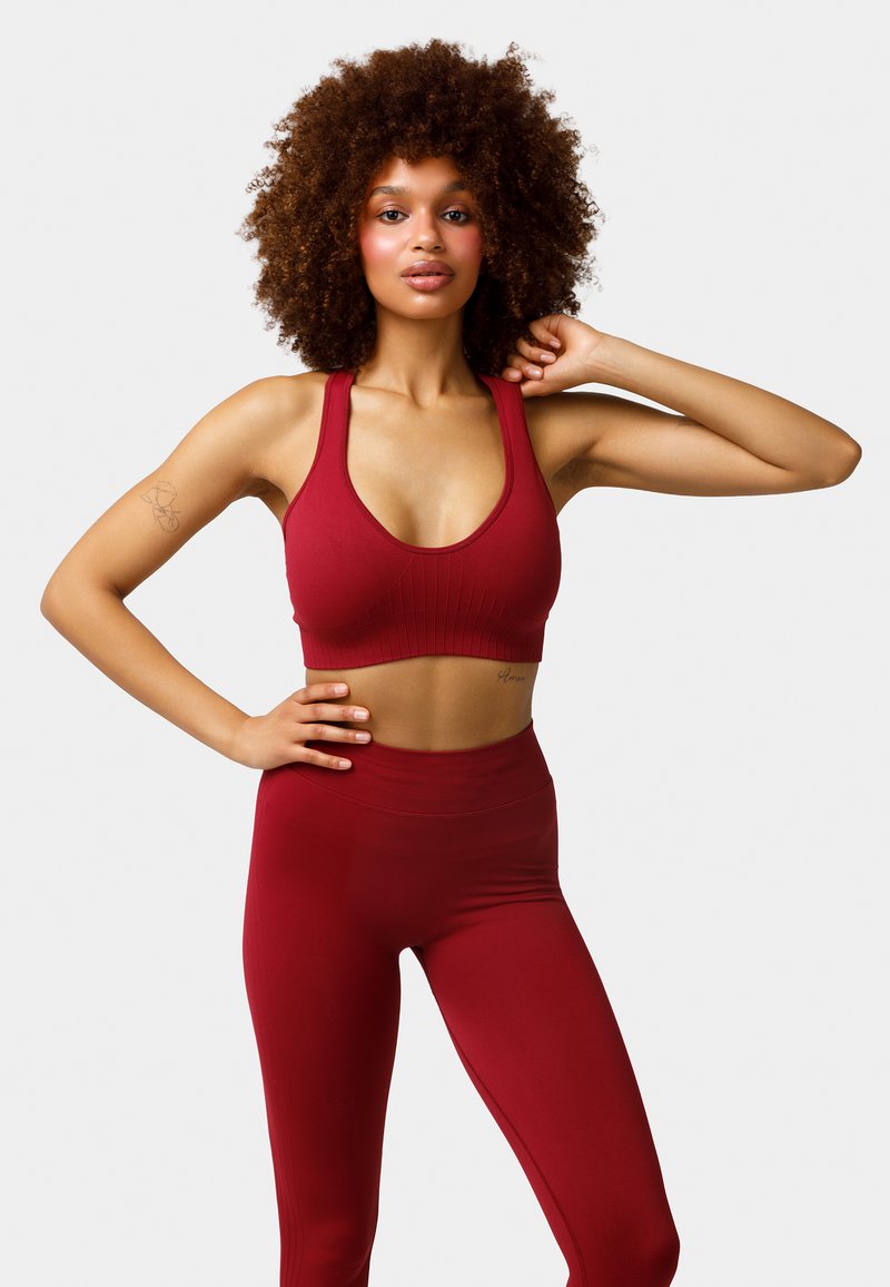 Sujeta deportiva roja con textura acanalada y tirantes anchos, combinada con leggings de cintura alta a juego. Ambas prendas están hechas de material elástico.
