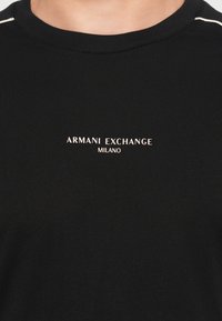 Svart bomull T-skjorte med rund hals som har "ARMANI EXCHANGE MILANO" i lyse farger på fronten. Glatt tekstur, enkel design.
