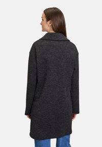 Donkergrijze jas van textiel met een grote kraag, lange mouwen en een rechte snit die onder de heupen valt.