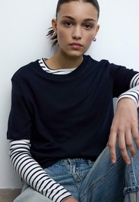 Marineblauw T-shirt met korte mouwen over een wit en marineblauw gestreept shirt met lange mouwen, gecombineerd met lichtblauwe denim jeans.